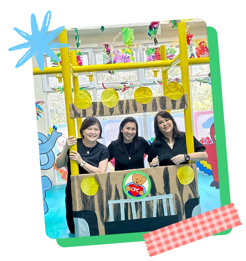 Three Creative Play Corner teachers smiling together at a vibrant school display booth