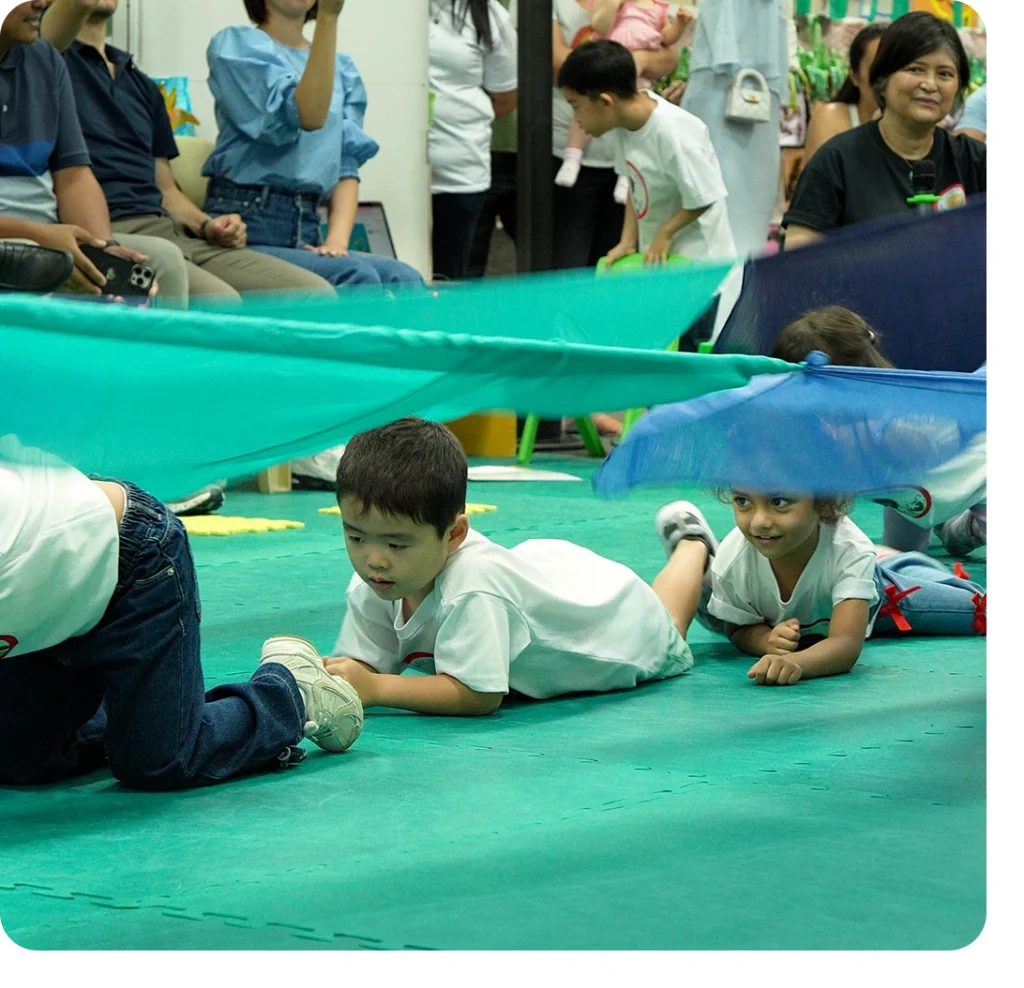 Children crawling under a large green parachute during a fun parent-participation activity at Creative Play Corner