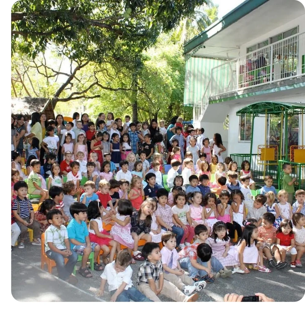 A large group of CPC children and parents gathered together outdoors in the school courtyard during a community event