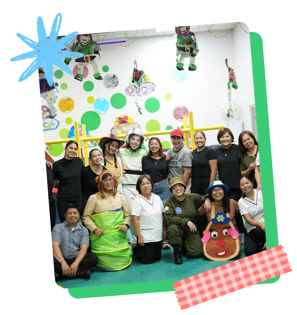 Creative Play Corner teachers and staff posing together in creative costumes under colorful hanging craft decorations